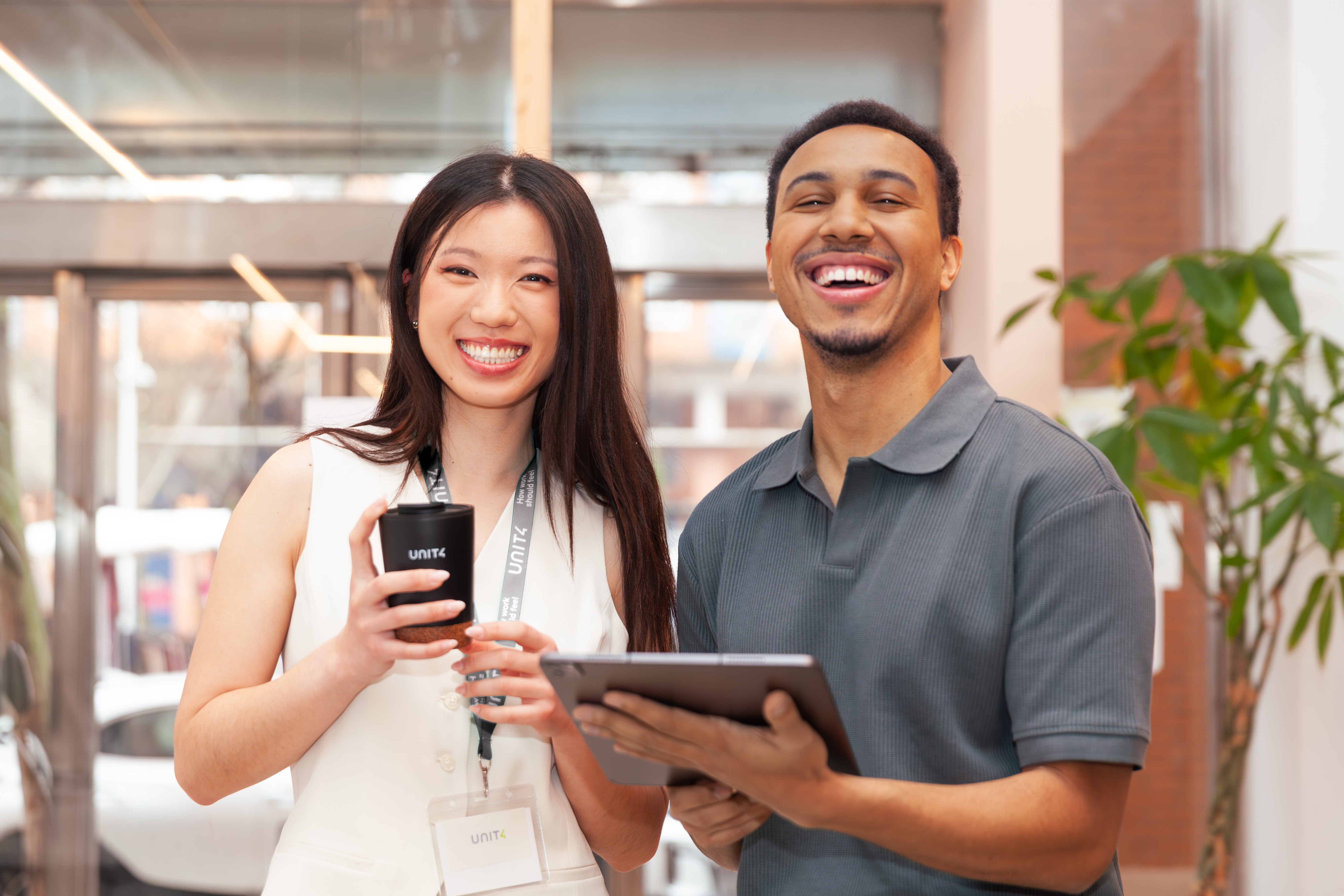 Two smiling colleagues standing side by side with a phone and tablet at work